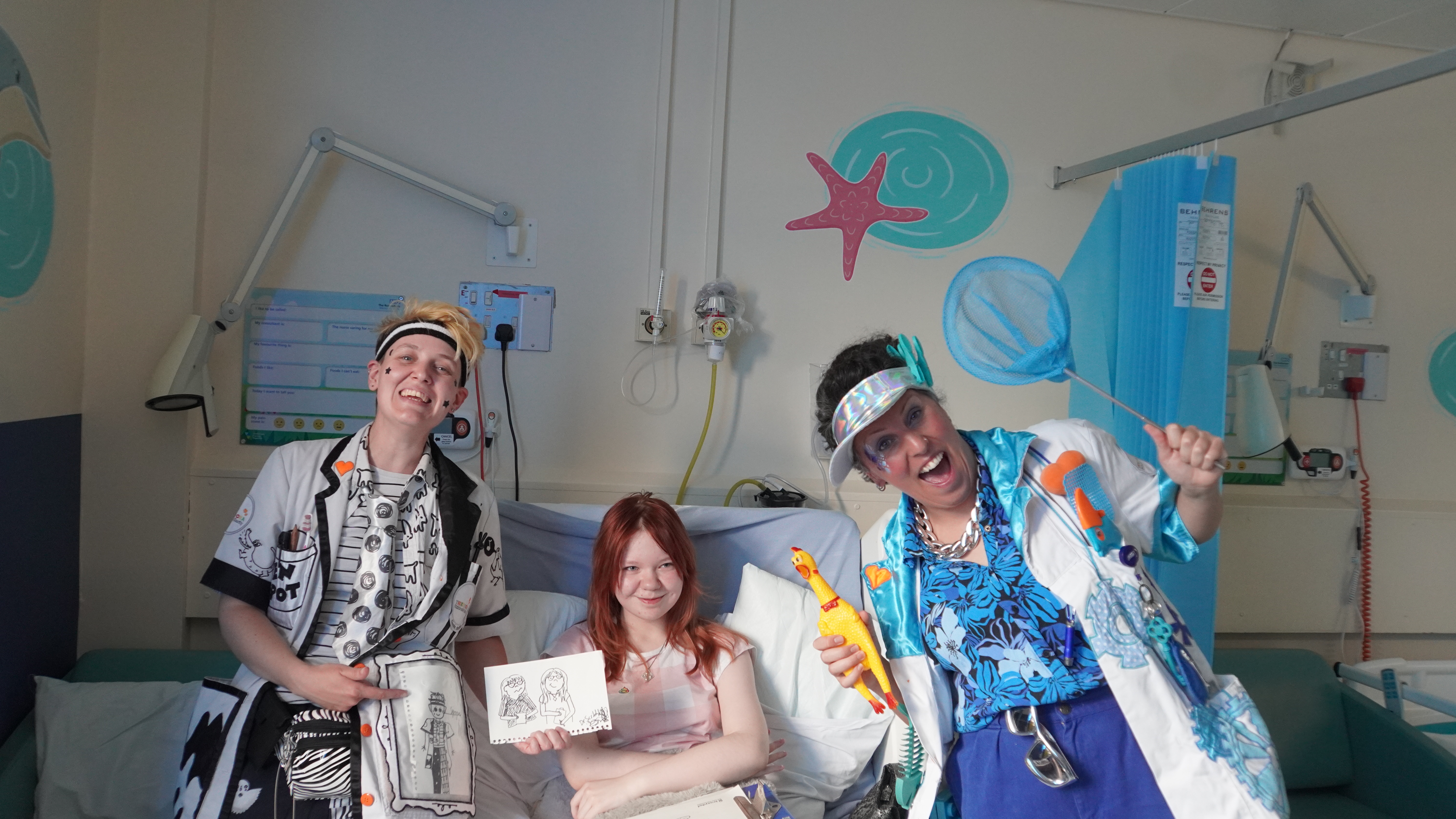 Two giggle doctors stood either side of a young girl in a hospital bed