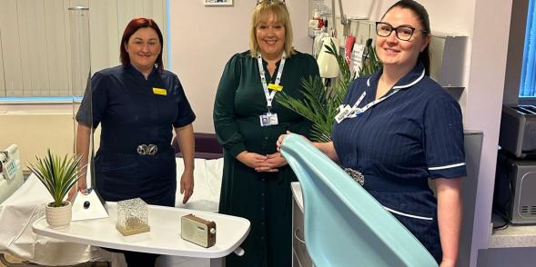 3 members of staff in one of the purple butterfly rooms, posing with newly funded charity items. 