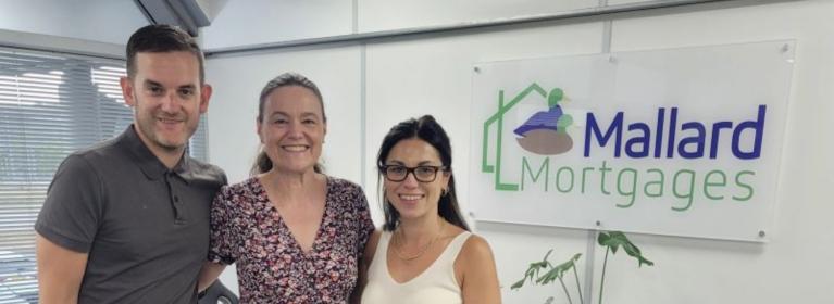 Rachael, head of fundraising at the charity posing with two staff members from Mallard Mortgages, with the Mallard Mortgages sign in the background. 