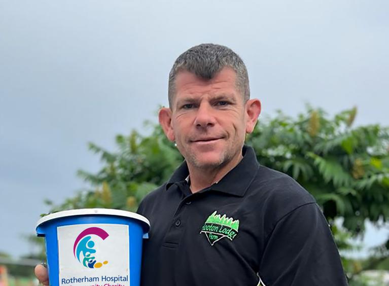 Man wearing a Hooton Lodge tshirt holding a collection bucket for Rotherham Hospital and Community Charity