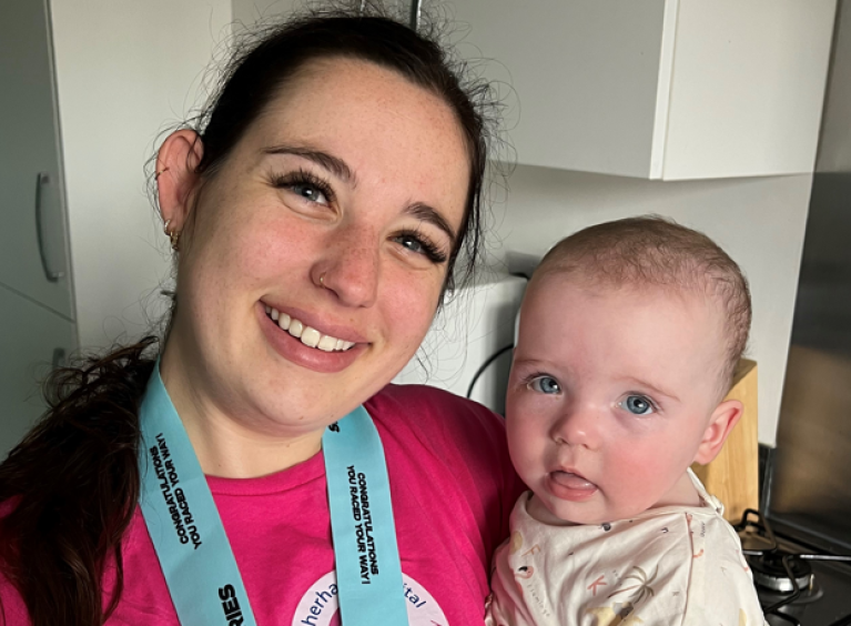 Erin Wyatt wearing a pink charity-branded t-shirt and medal, holding baby Erin