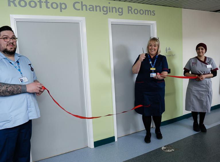 Chief Nurse, Cindy Storer, cuts a red ribbon held by two healthcare support workers to open some new changing rooms