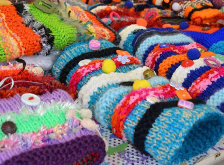 Display of 10 colourful twiddlemuffs. Some have bows, zips, and buttons sewn on. 