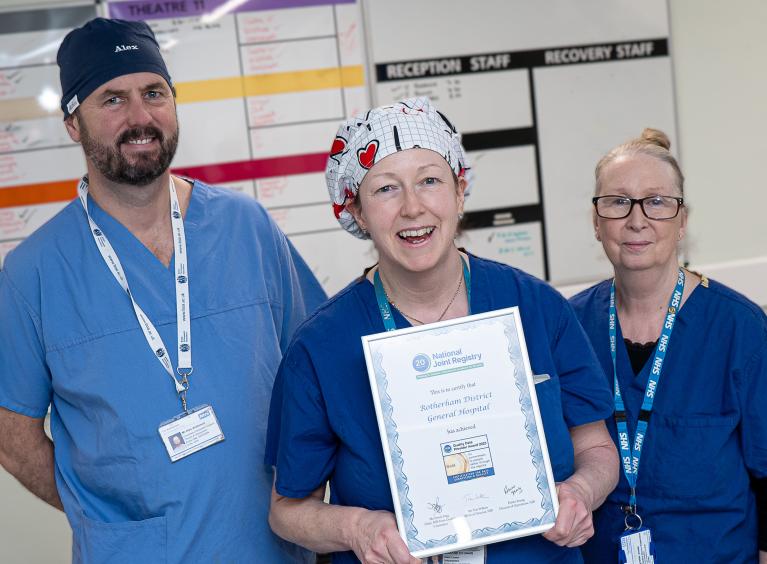 Surgeon and theatre staff pose holding a certificate