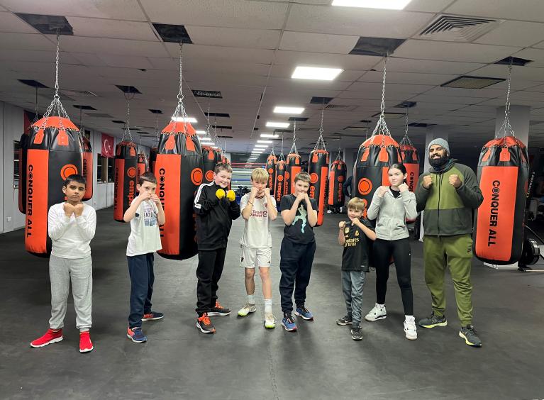 Six children and an adult pose with boxing bags