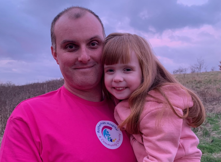 A father and daughter. The father is wearing a pink charity t-shirt.