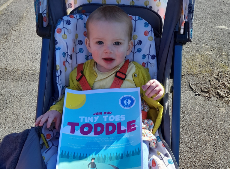 A toddler in a pushchair with a flier for the Tiny Toes Toddle