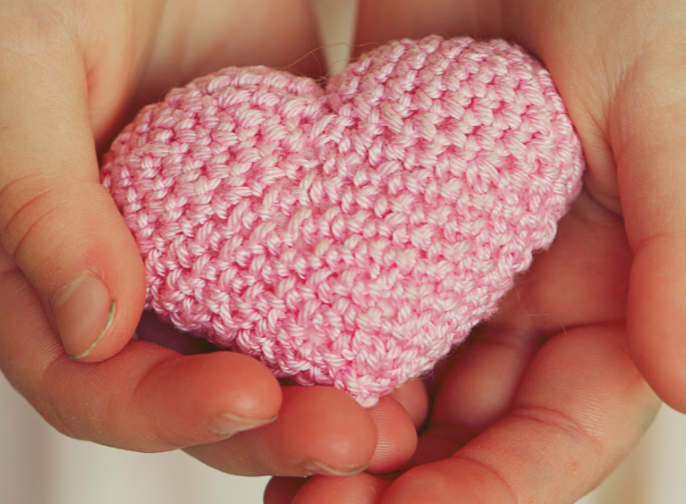 A pink crocheted love heart in someone's hands