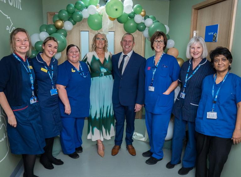 A group of neonatal unit staff and two members of the public stood at the entrance to the neonatal unit under a green balloon arch