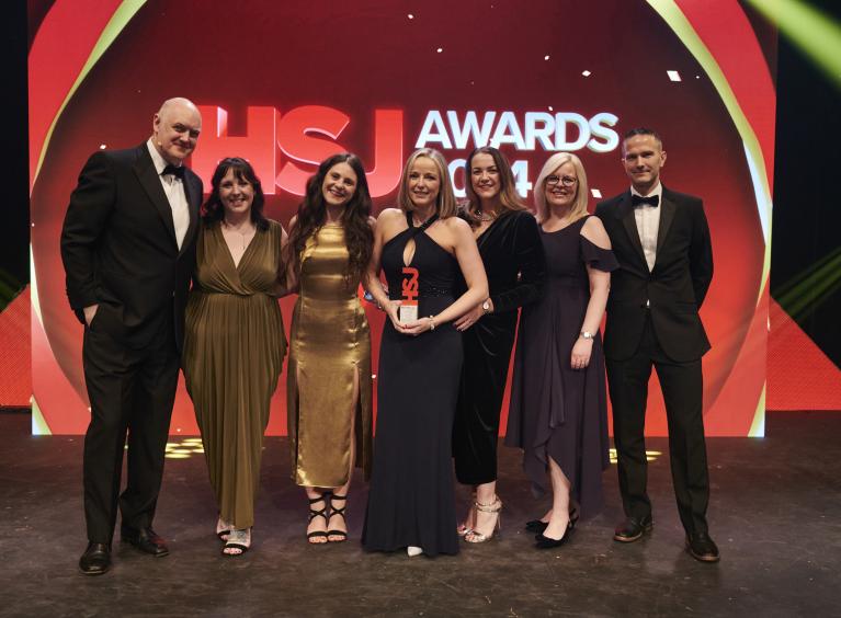 Seven people stood in front of a backdrop that says HSJ Awards 2024. One of the people is holding a trophy