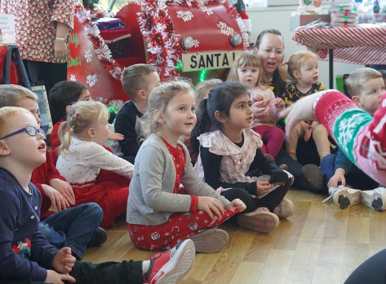A group of young children sat on the floor in front of Santa's sleigh