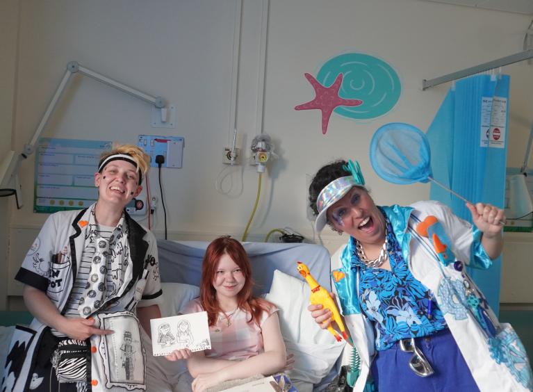 Two giggle doctors stood either side of a young girl in a hospital bed