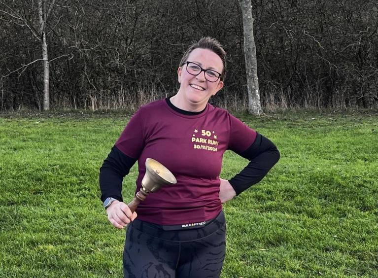 Barbara is in a park smiling and ringing a bell