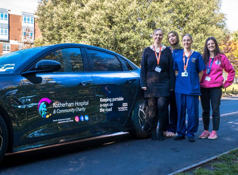 Four members of staff stood next to a car with the Trust's and charity's logo on the side.