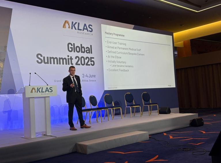 A man is stood on a stage. The backdrop says 'KLAS Global Summit 2025'