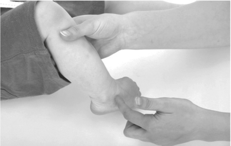 A person is supporting a baby's calf with one hand and tickling the outside of the baby's foot with their other hand