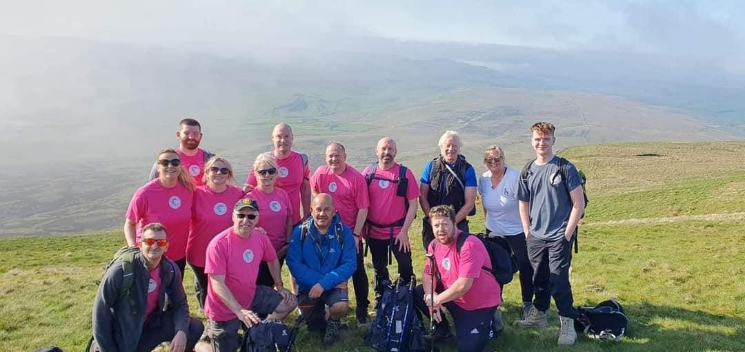 Team of people undertaking the Three Peak Challenge in 2023, many wearing pink charity t-shirts, stood on a hill.