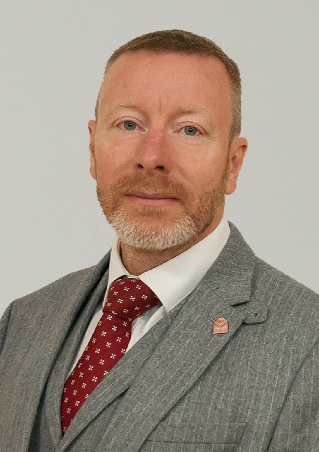 Gavin Rimmer wearing a grey suit with a red tie