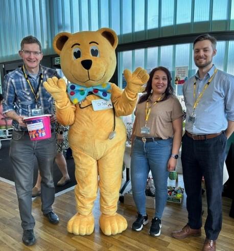 A group of corporate volunteers helping out at a charity event, posing with Dr Ted, the charity mascot.