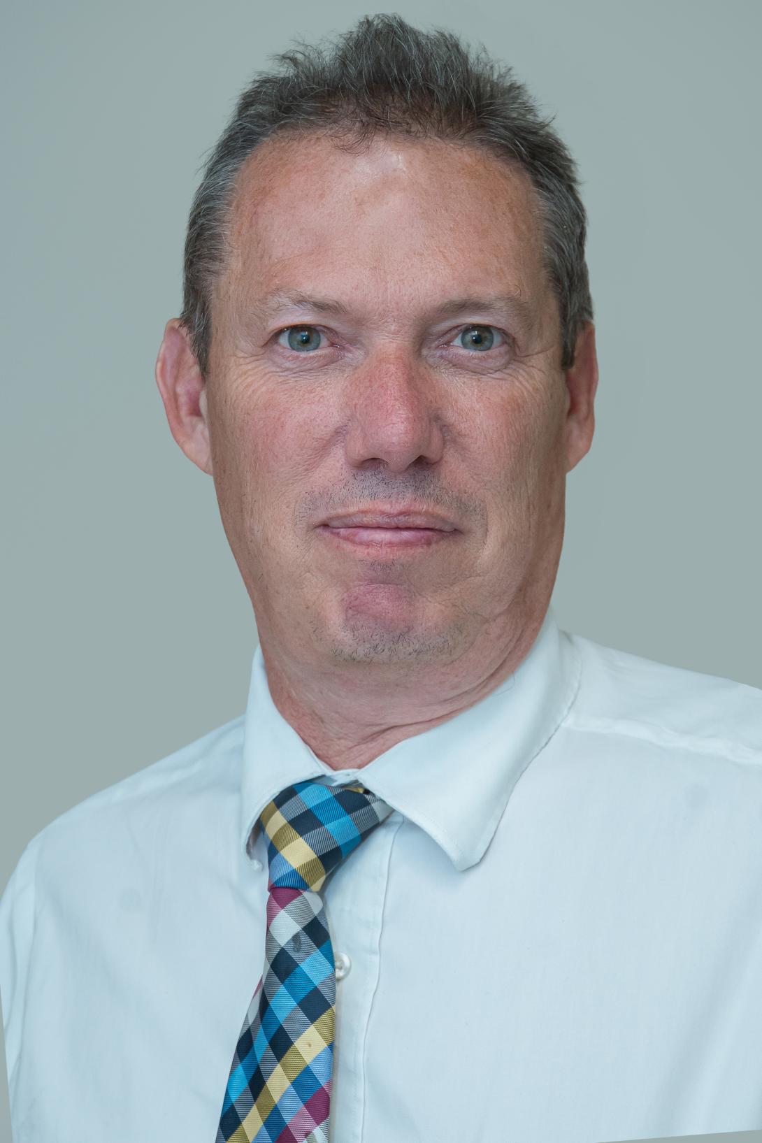 Andrew is wearing a white shirt and multi-coloured chequered tie