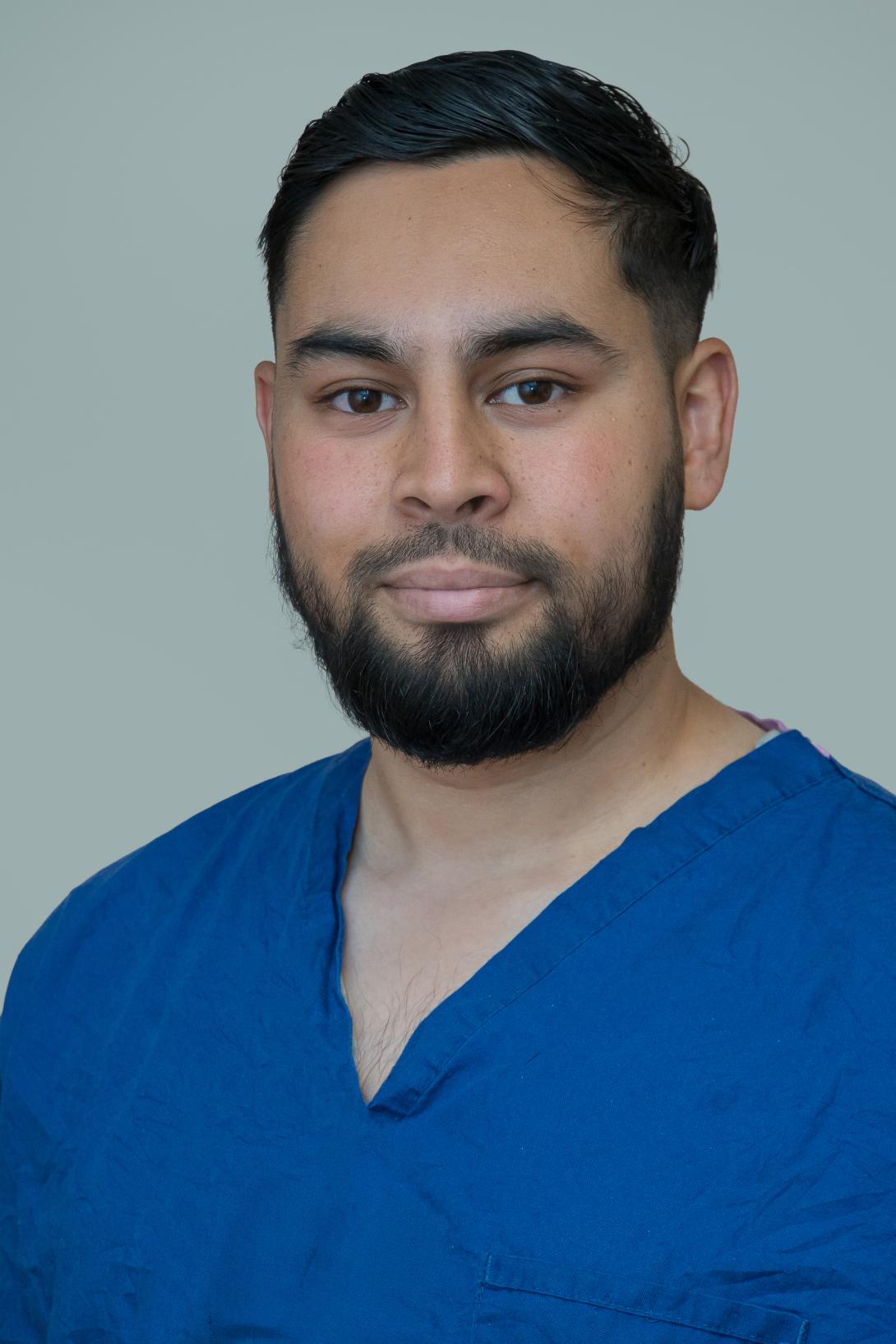 Hamza has a beard and is wearing a blue scrub top